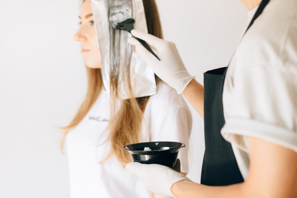 pexels-photo-8468125 Hairdresser applying color to woman's hair in salon using brush and foil technique.